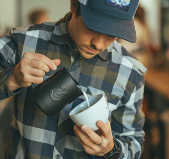 Ein Mann füllt Milch zu einem Kaffee